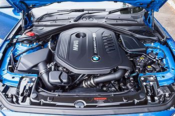 The engine of a blue bmw is shown with the hood open.