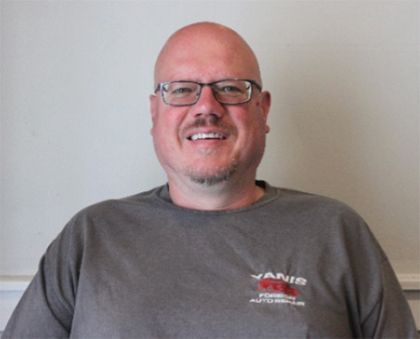 A bald man wearing glasses and a vanis shirt smiles for the camera