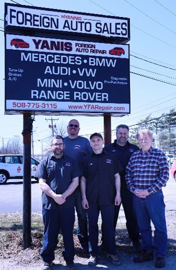 A group of men standing in front of a sign for foreign auto sales