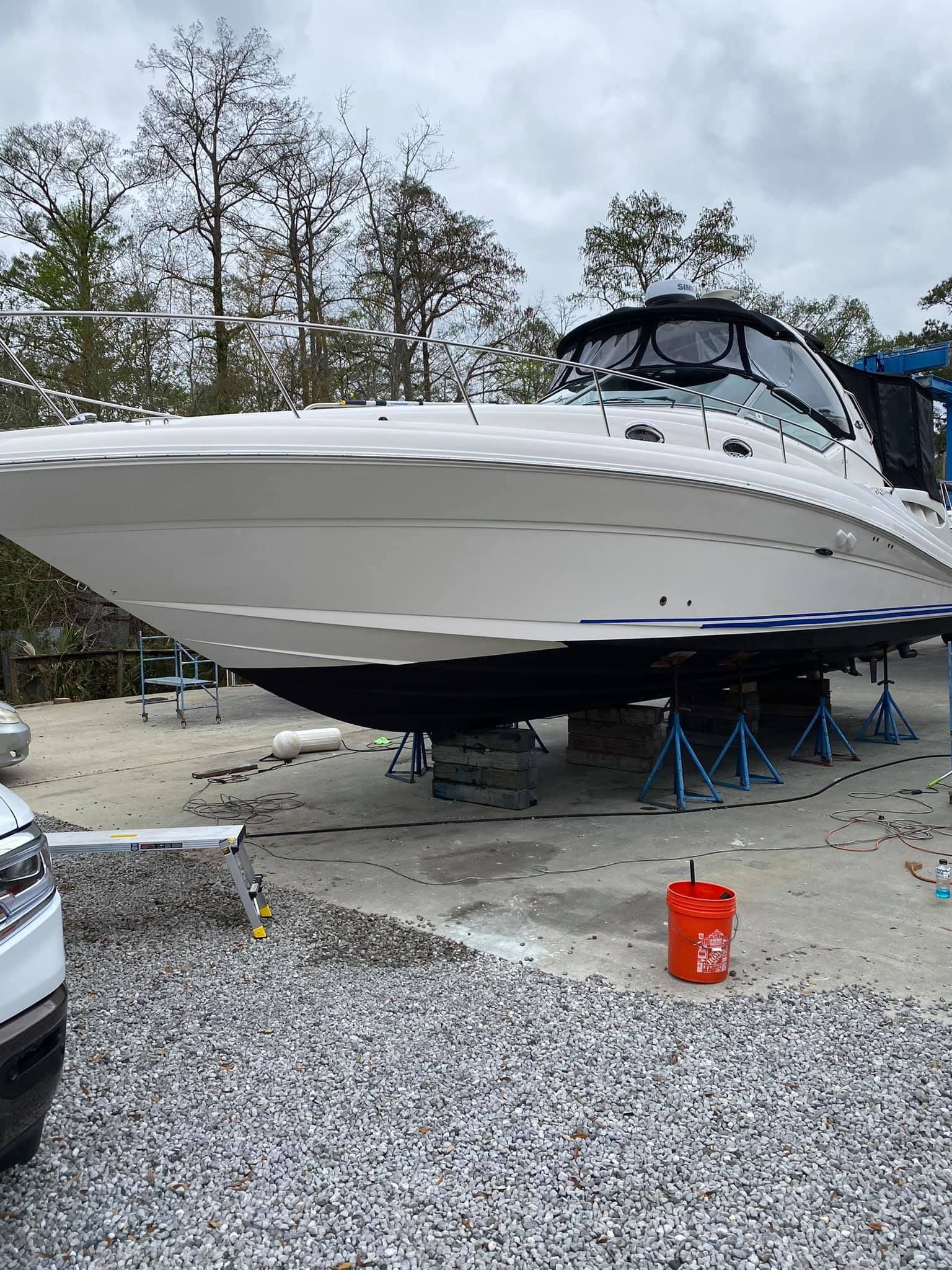 A boat is sitting on a trailer in a gravel lot.