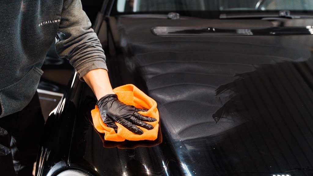 A person is cleaning the hood of a black car with a cloth.