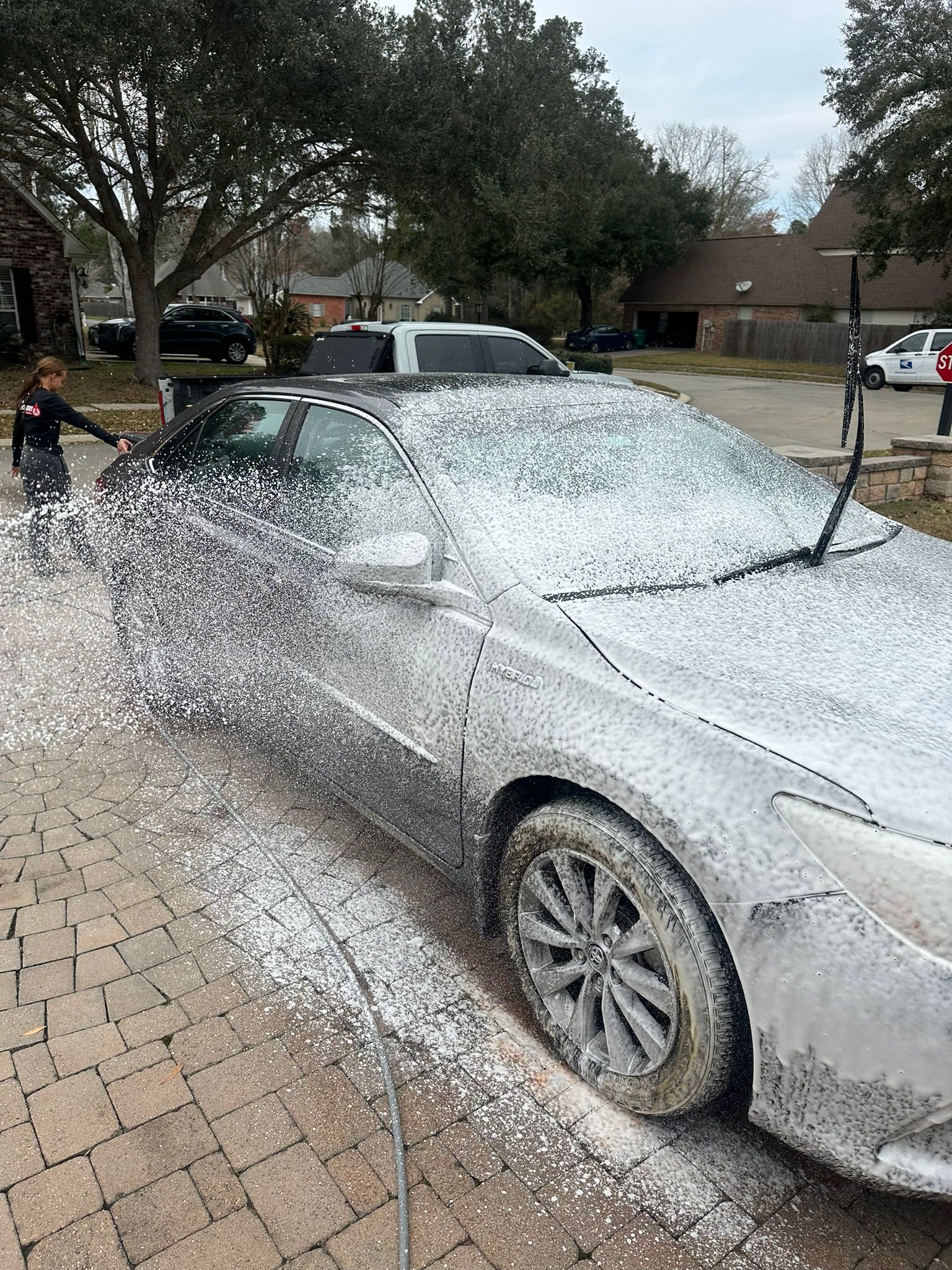A car is covered in foam and a child is standing next to it.