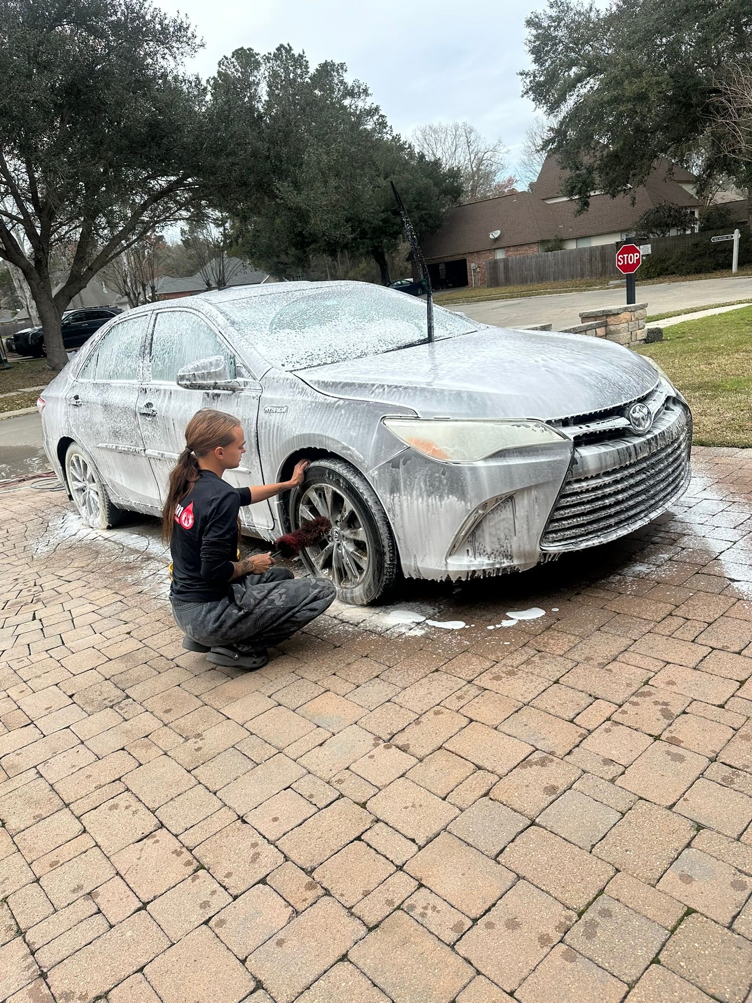 A woman is kneeling down next to a car covered in foam.
