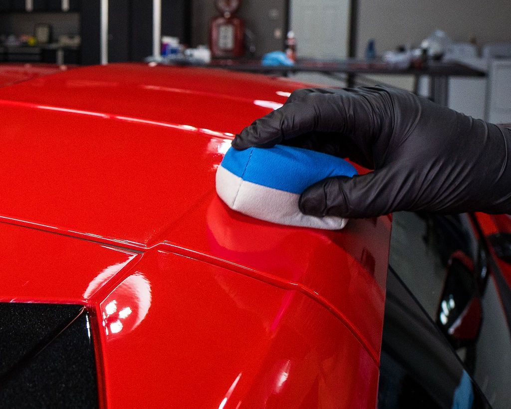 A person is polishing a red car with a blue and white sponge.