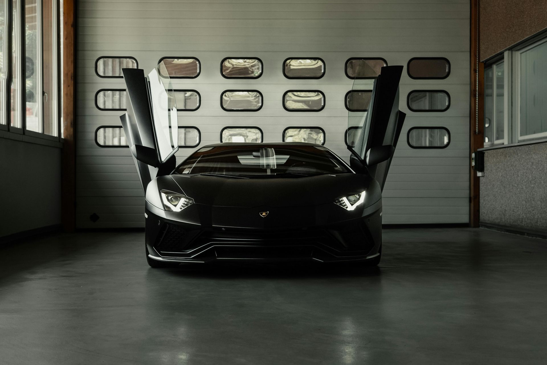 A black sports car is parked in a garage with its doors open.