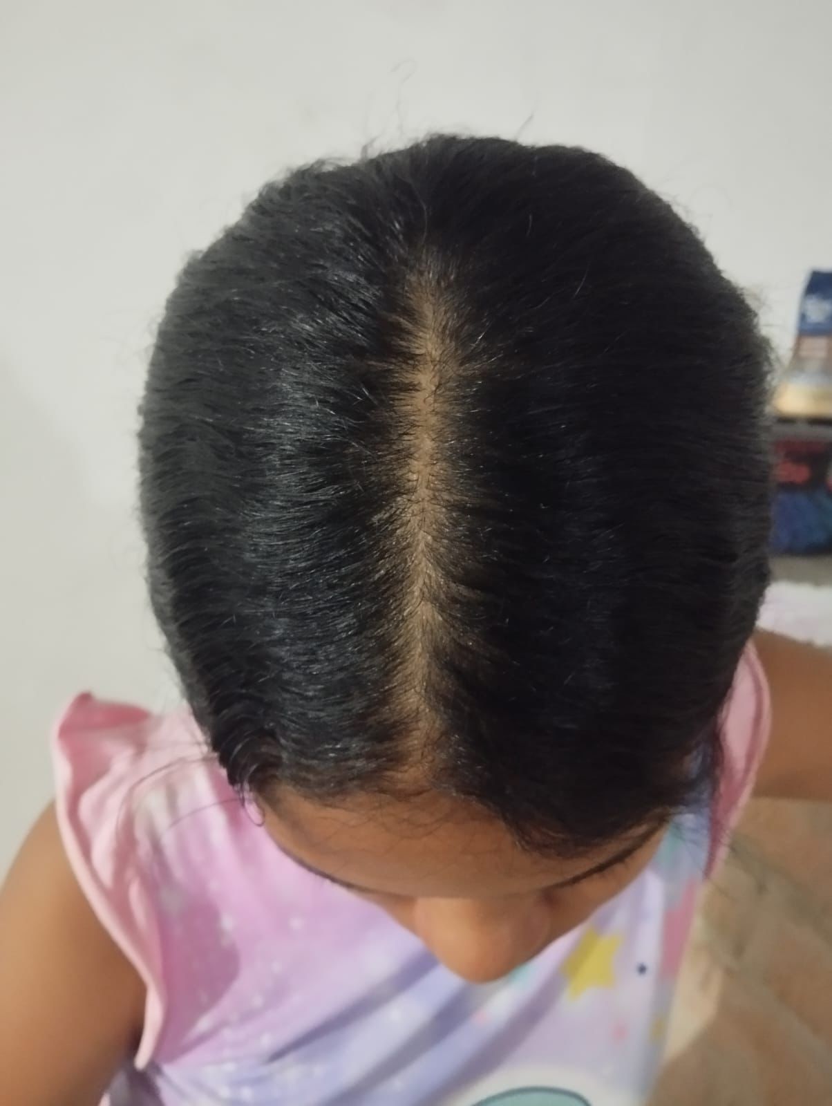 Primer plano, tomado desde un ángulo elevado, del cabello oscuro y rizado de una persona, peinado con un accesorio floral rosa y la raya al lado.