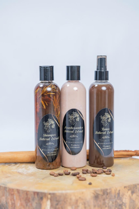 Tres frascos de productos naturales para el cuidado de la piel con etiquetas negras reposan sobre una superficie de madera junto a granos de café y canela.