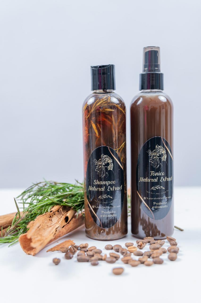 Dos frascos transparentes de líquido de hierbas con etiquetas oscuras, rodeados de granos de café, ramas de canela y romero esparcidos.