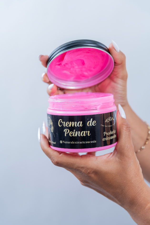 Una persona sostiene un frasco abierto de crema para peinar el cabello de color rosa brillante con una etiqueta negra, frente a un fondo liso.
