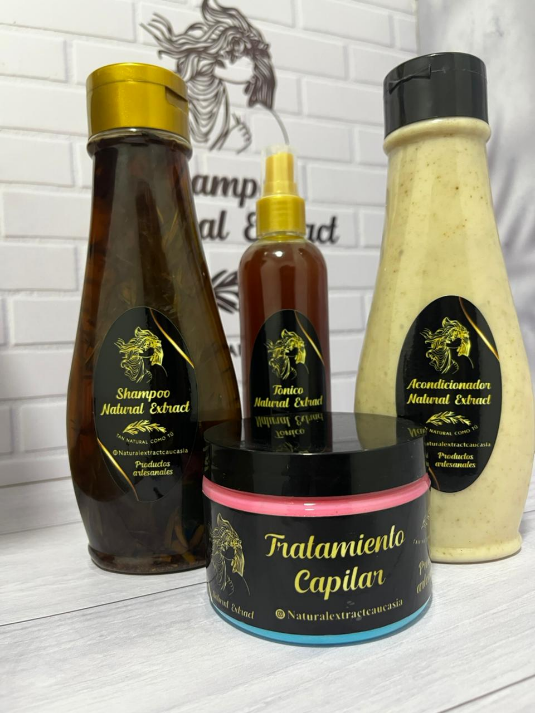 Un champú, un tratamiento capilar, un spray y un acondicionador se disponen sobre una superficie de madera blanca con una pared de ladrillos de fondo.