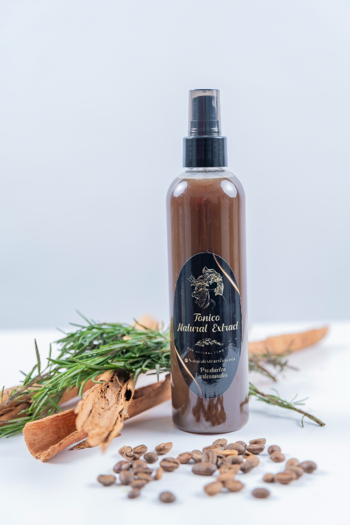 Un pulverizador marrón reposa sobre una superficie blanca con ramitas de romero, palitos de canela y granos de café esparcidos.