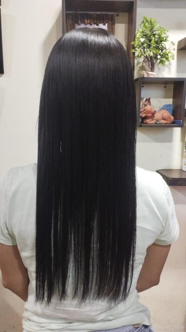 Vista trasera de una persona con cabello largo, liso, negro y brillante que le llega hasta la mitad de la espalda, y que viste una camisa de color claro.