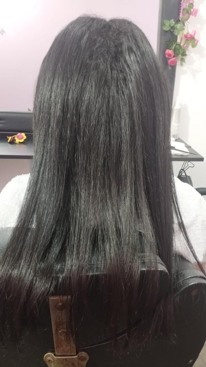Vista posterior de una melena larga, lisa y oscura con textura visible producida por el uso de herramientas de calor, en un salón de belleza.