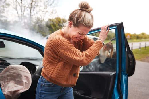 A woman is standing next to a broken down car.