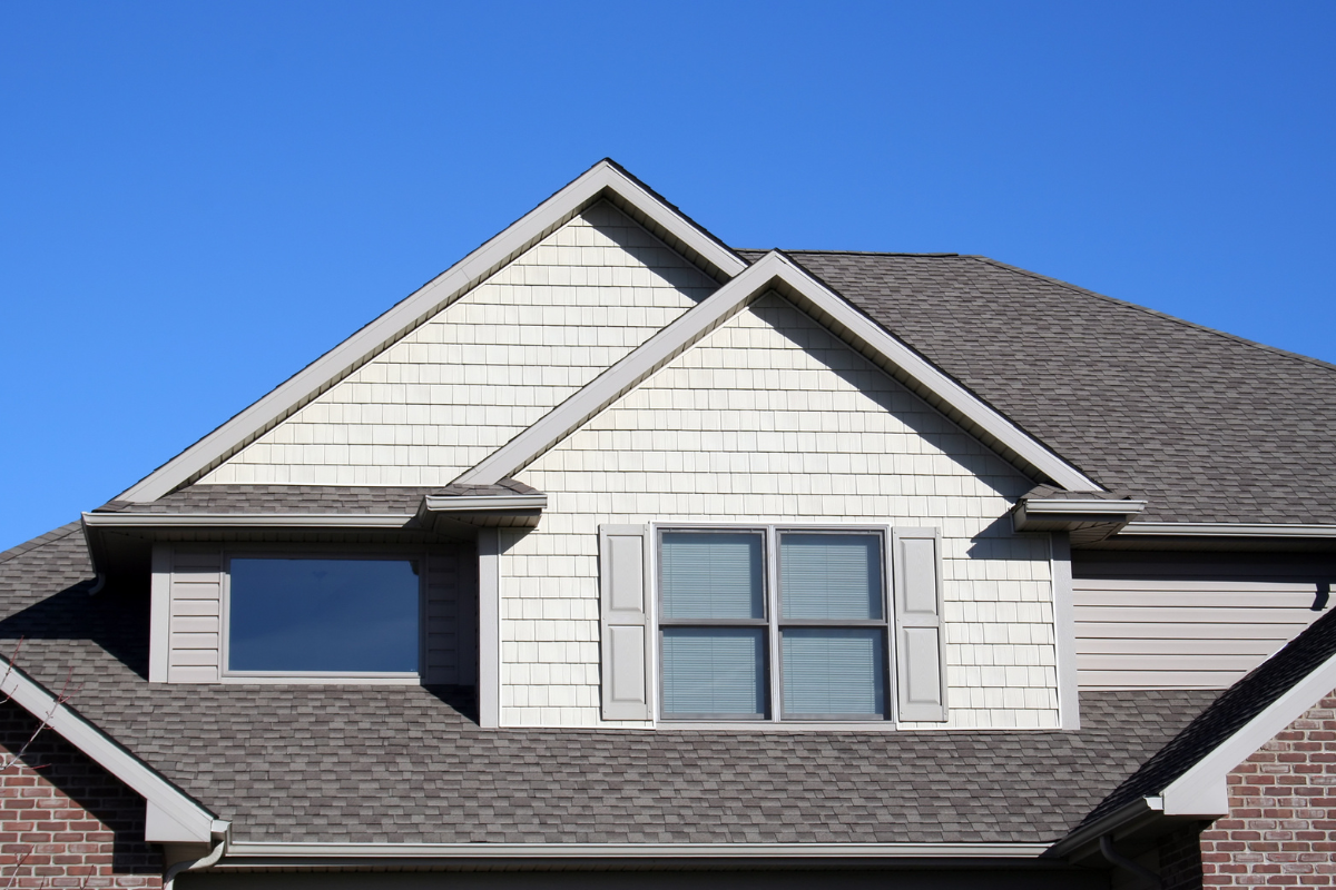 The roof of a house with a window and a blue sky in the background.