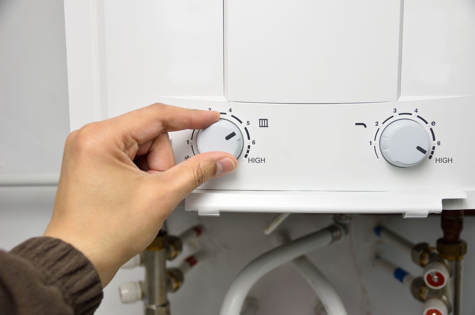 A person is adjusting a thermostat on a boiler.
