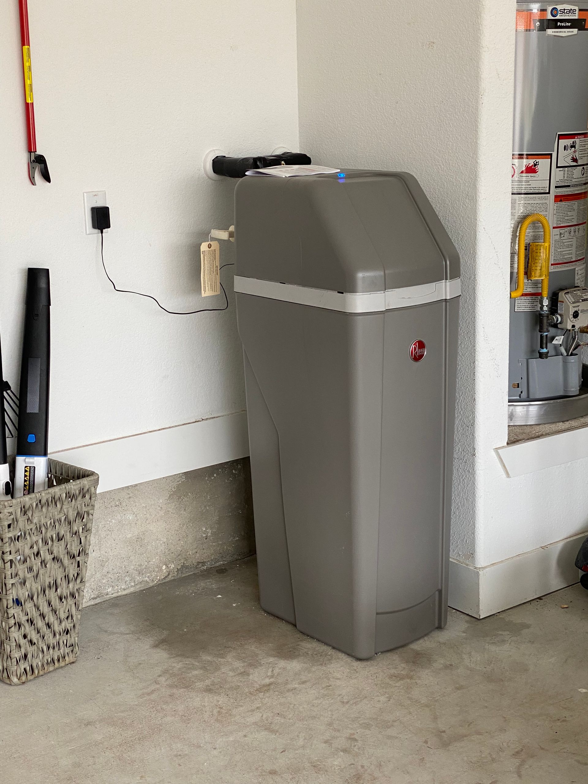 A gray trash can is sitting in a corner of a garage.