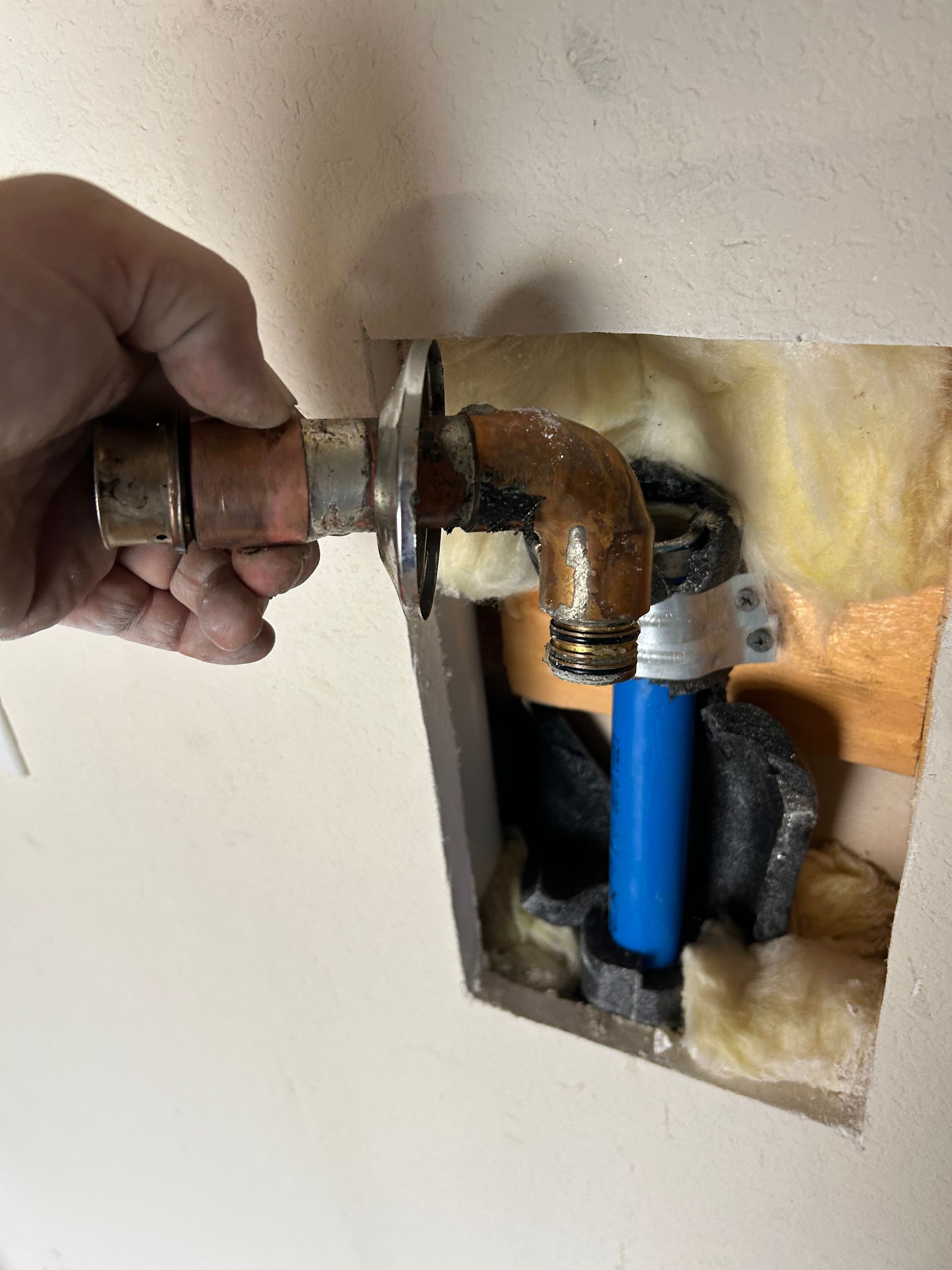 A person is holding a pipe in a hole in the wall.