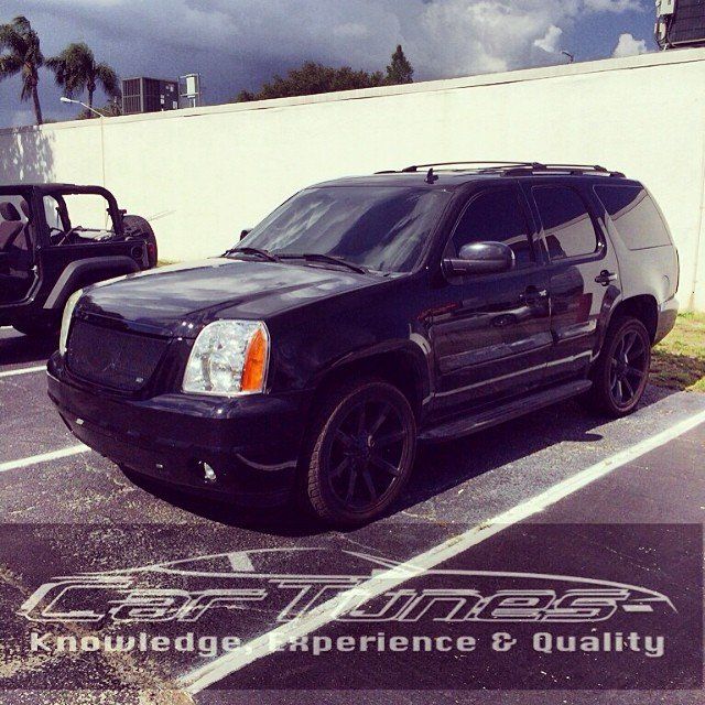 Black GMC Yukon SUV with tinted windows and black wheels parked in a parking lot.