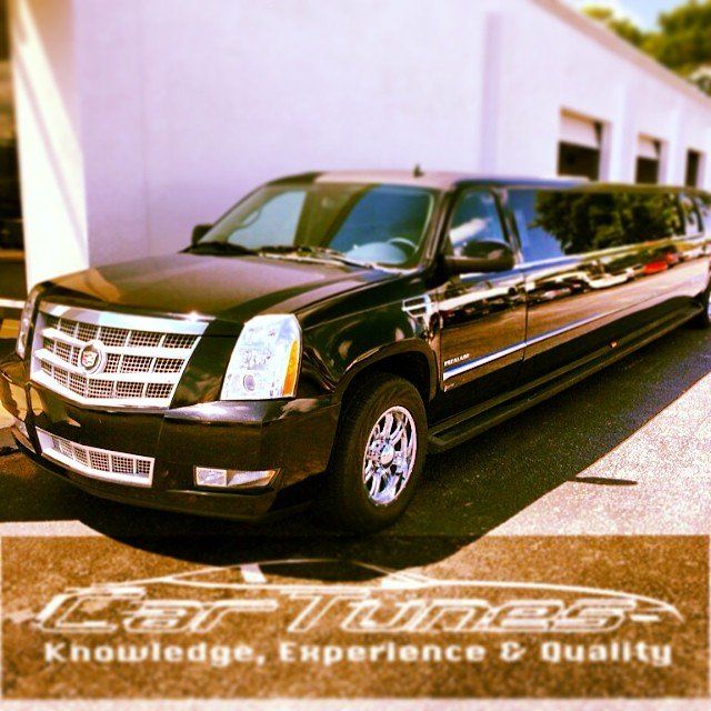 Black Cadillac Escalade limousine parked in front of a white building.