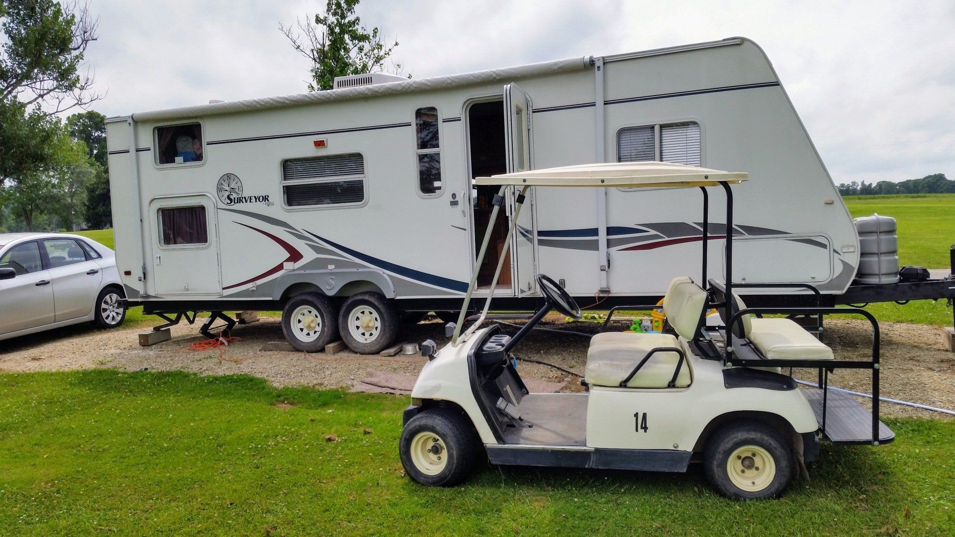 White RV trailer with a golf cart parked in front of it on a grassy field.