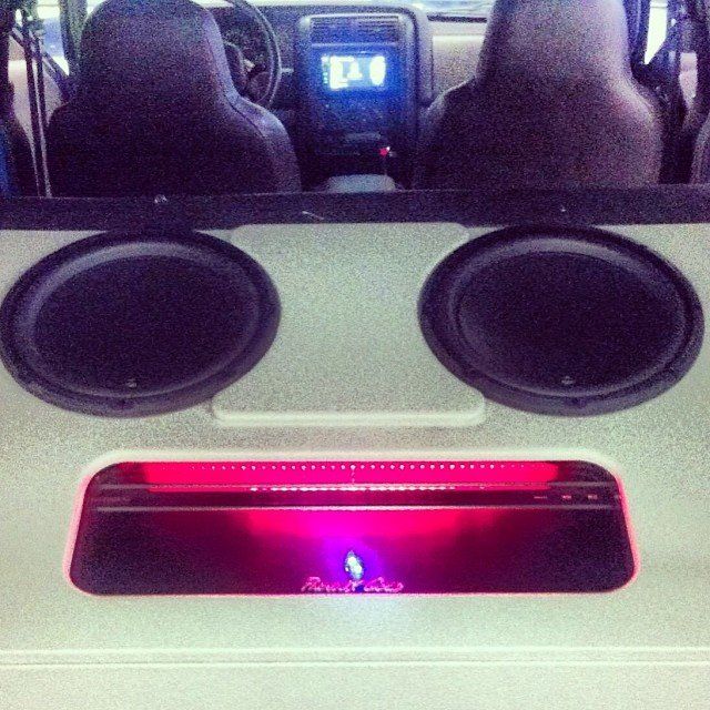Two large black speakers and a lit red amplifier in a vehicle's interior.