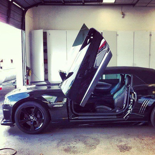 Black convertible car with doors open upwards inside a garage.
