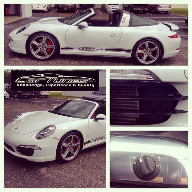 White Porsche Targa convertible car with red brake calipers, black stripes, and logo, parked outdoors.