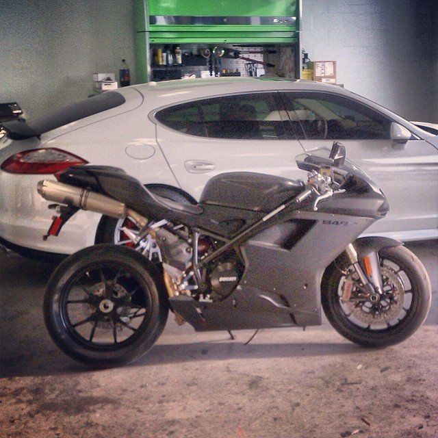 Gray motorcycle parked in front of a white car in a garage.