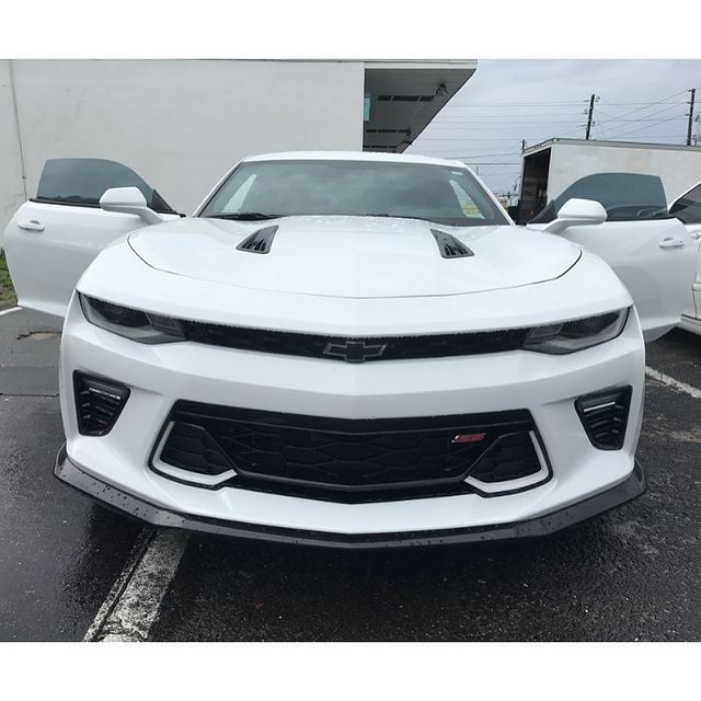 White Chevrolet Camaro with doors open, parked in front of a building.