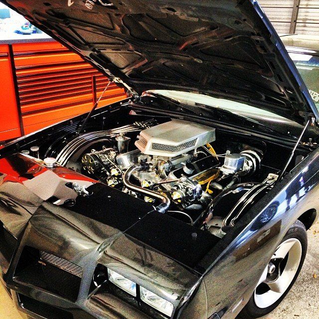 Black classic car with hood open, showcasing its chrome engine.