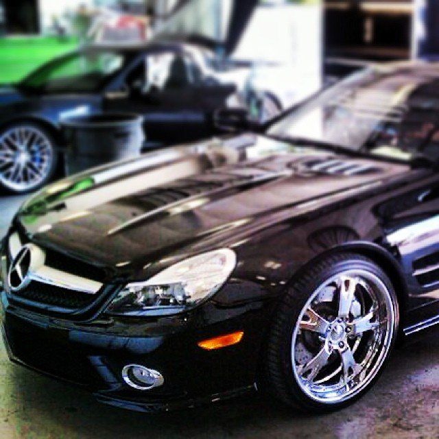 Black Mercedes SL with chrome wheels in a garage, another car in the background.