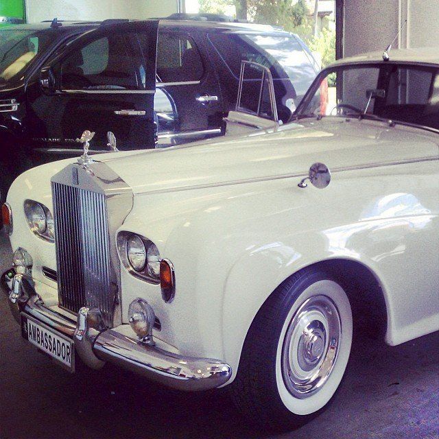 White Rolls Royce in front of a black SUV in a garage setting.