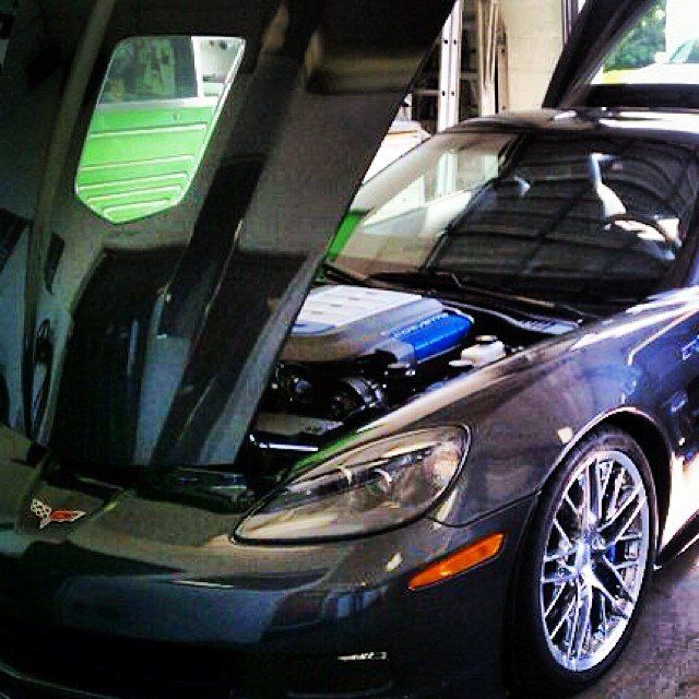 Gray Corvette with the hood up, revealing a blue engine, parked in a garage.
