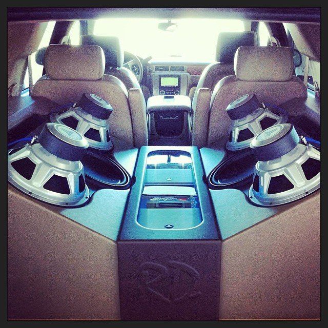 Interior of a car modified with two large subwoofers, an amplifier, and tan leather seating.
