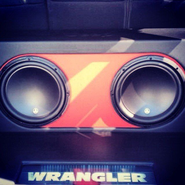 Two large black subwoofers in a car with an orange design over a black panel.