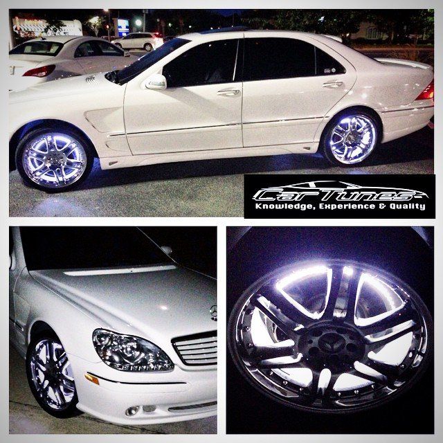 White car with blue underglow, custom rims, and logo.