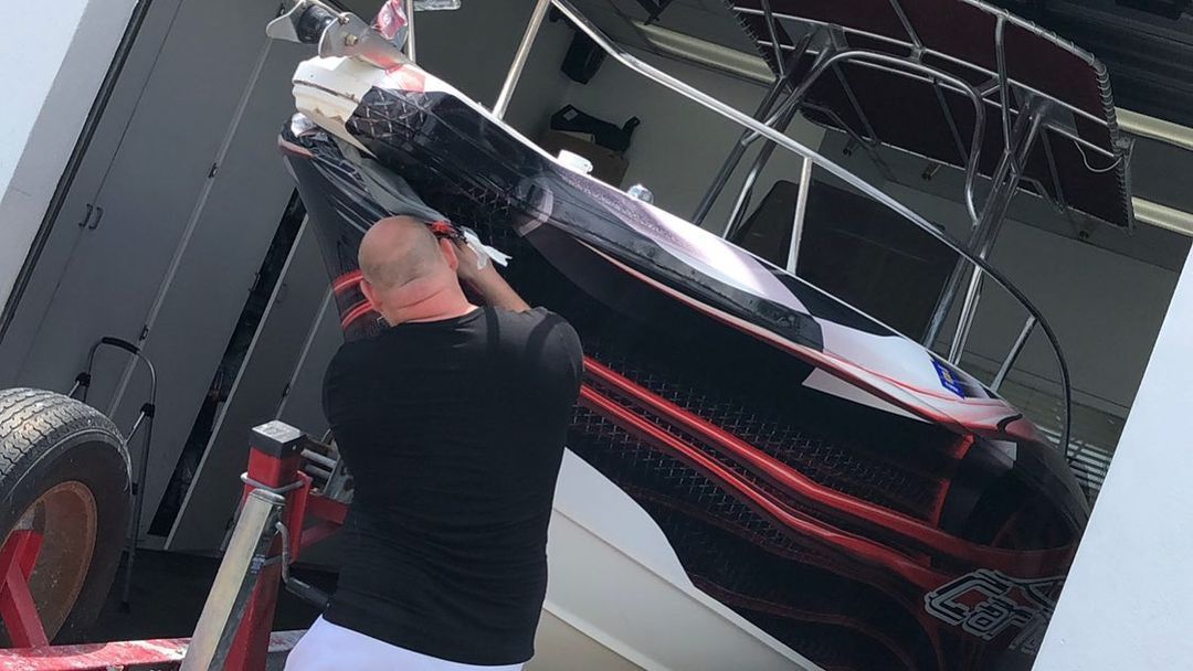 Man in black shirt loading a boat with black and red design onto a trailer.