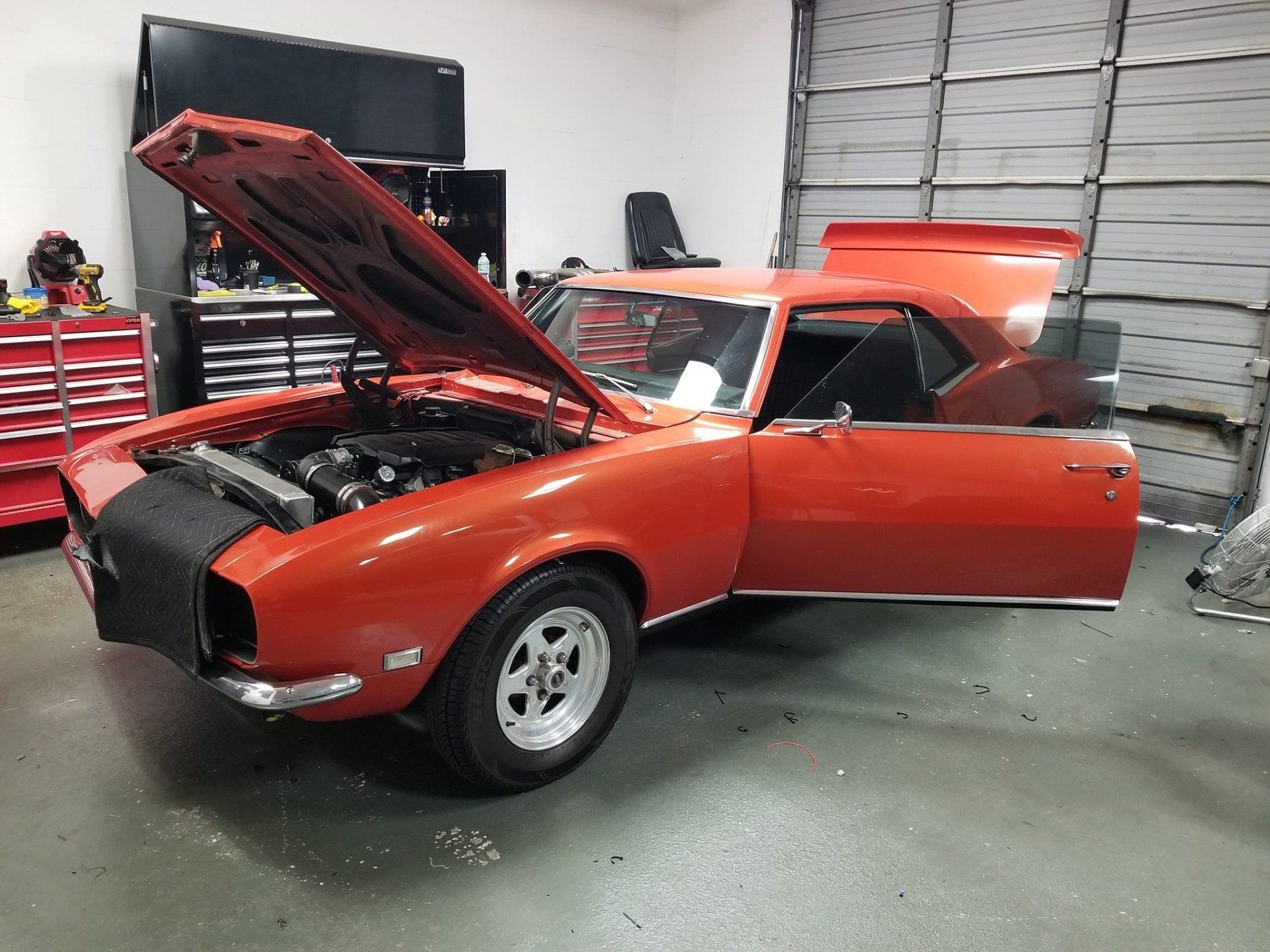 Orange classic car in a garage, with the hood, door, and trunk open.