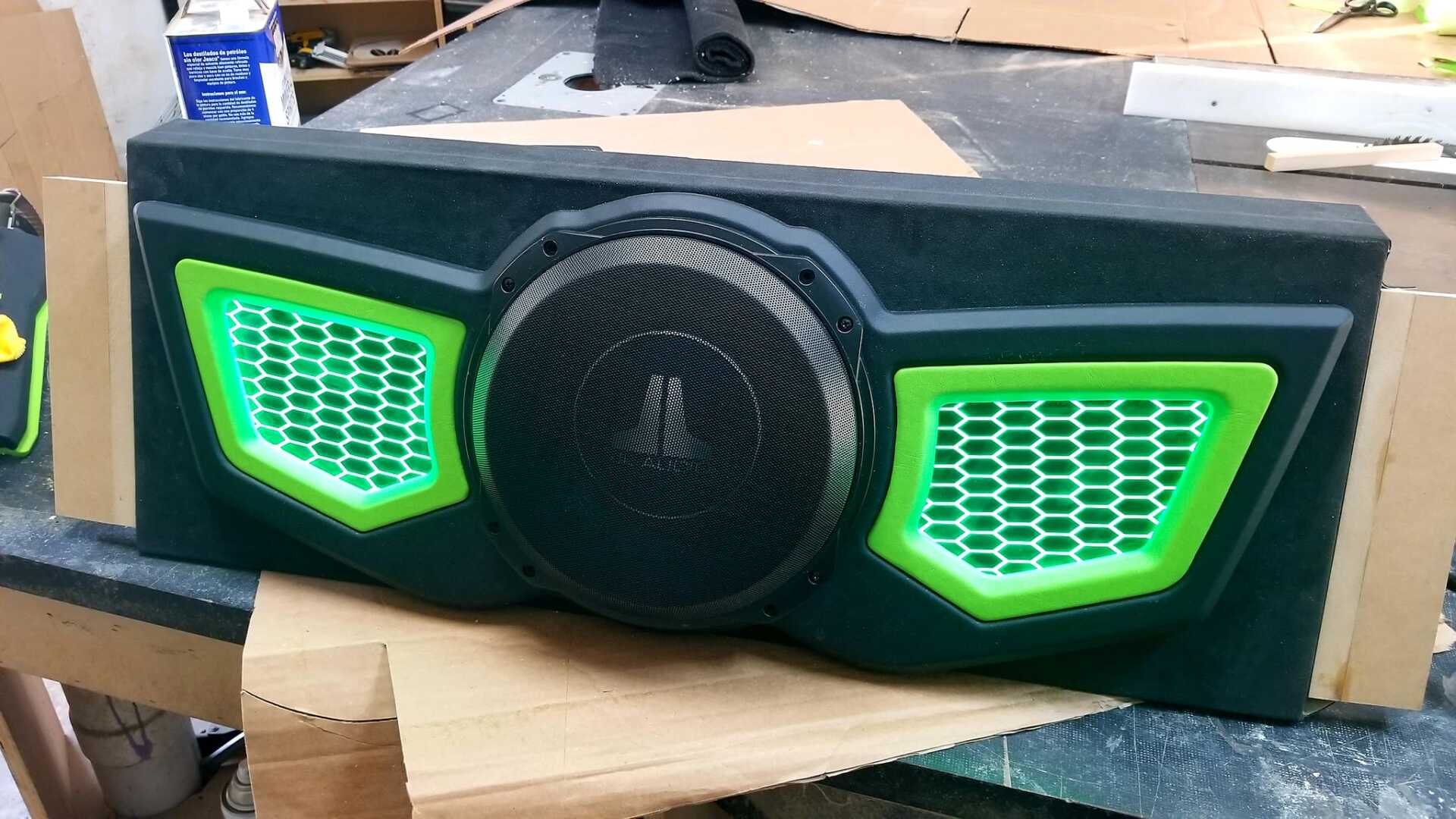 Black and green subwoofer box with illuminated green honeycomb accents.