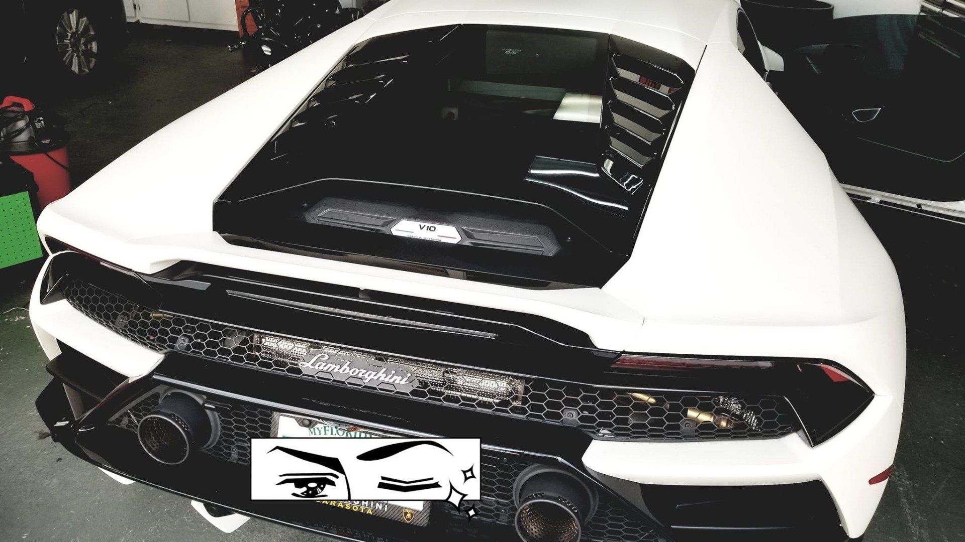 White Lamborghini sports car with black accents, rear view. In a garage setting.