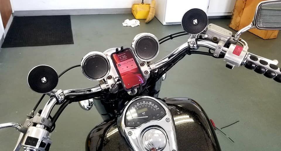 Motorcycle handlebars with a phone, two round speakers, and mirrors. Instrument panel visible.