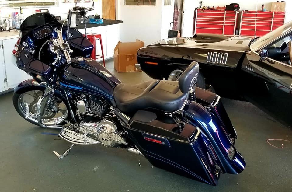 A dark blue custom Harley-Davidson motorcycle parked in a garage, next to a black muscle car.