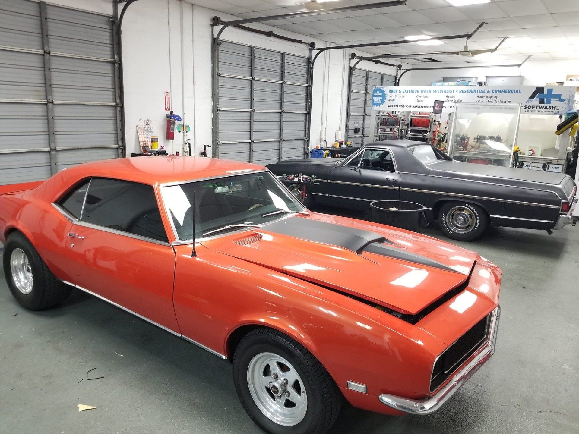 Red Camaro and black El Camino inside a garage.