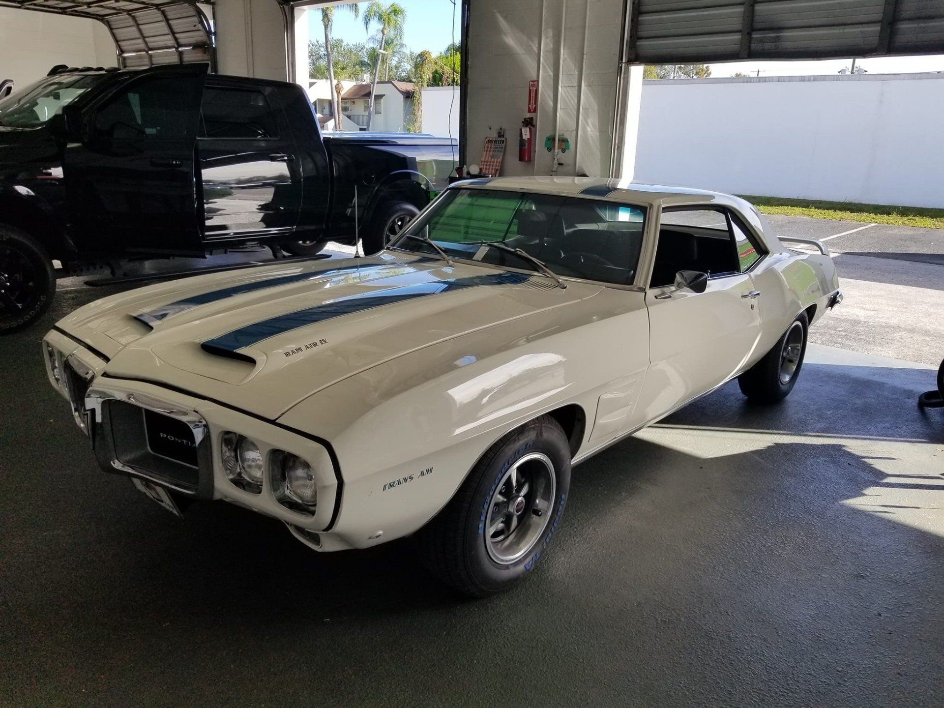 White 1969 Pontiac Firebird with blue stripes parked inside a garage.