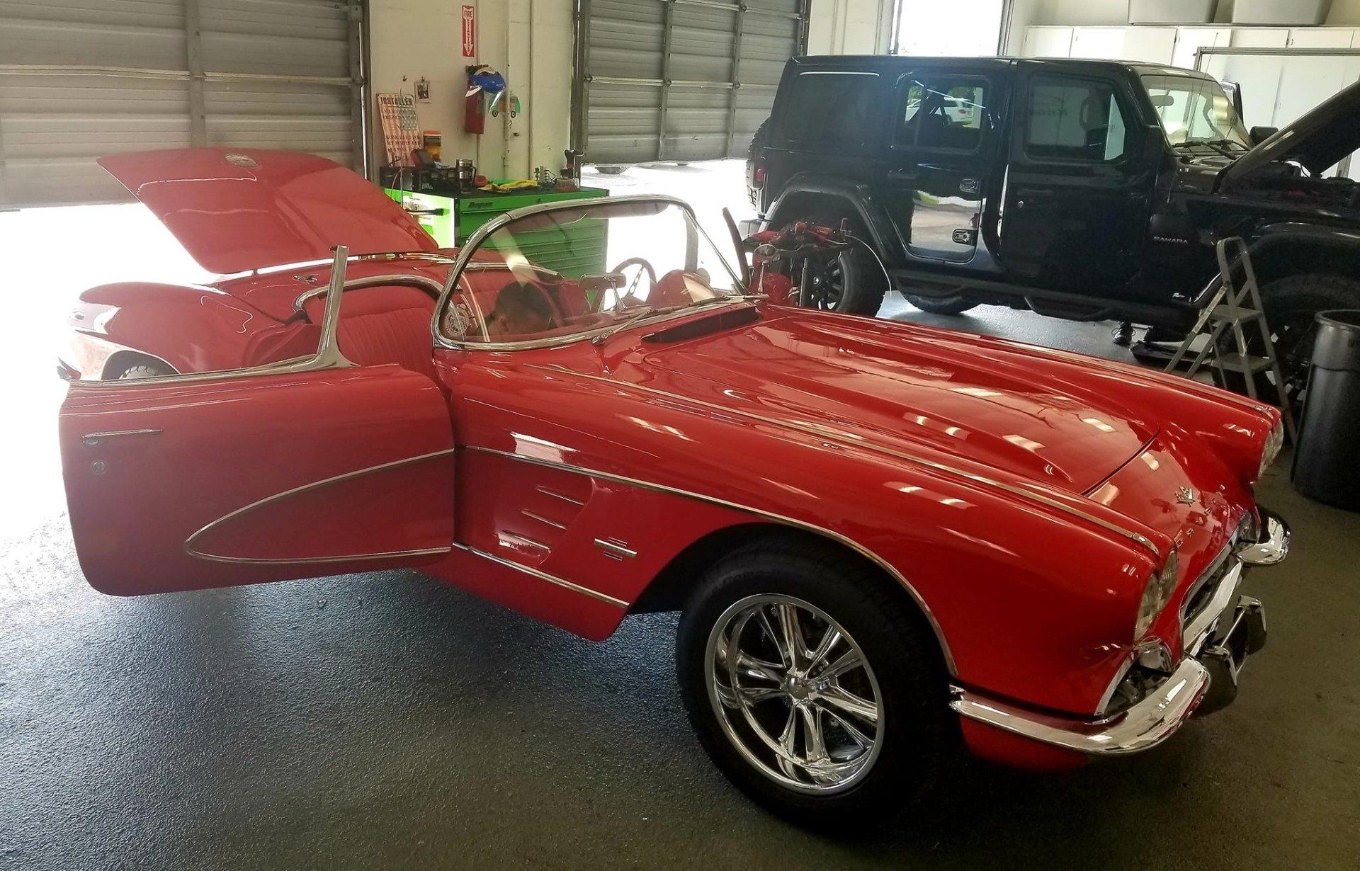 Red vintage convertible car with open doors and hood in a garage.