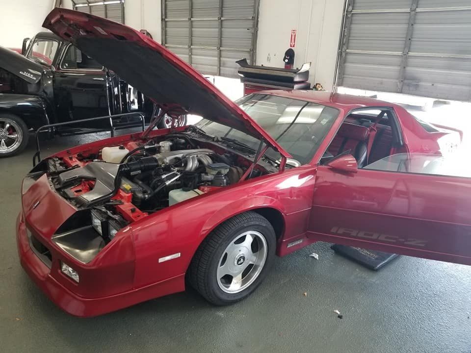 Red sports car with open hood and door in a garage, possibly being worked on.