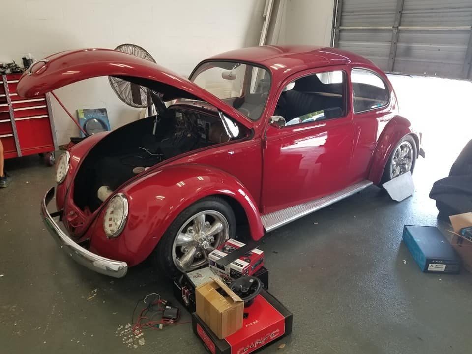 Red Volkswagen Beetle with the hood open in a garage, parked next to a device.