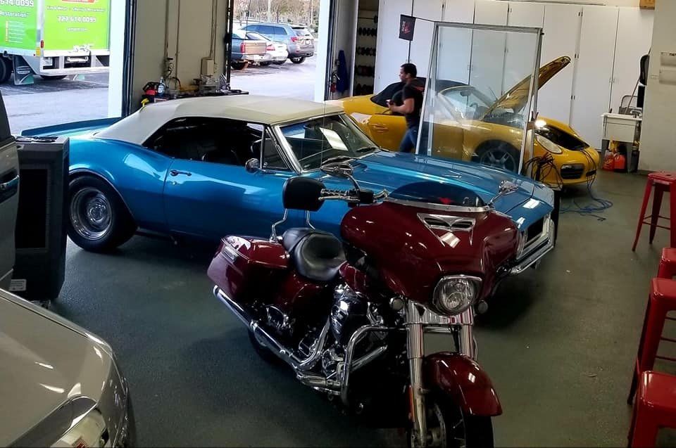 A red motorcycle in front of a blue convertible and a yellow sports car inside a garage.