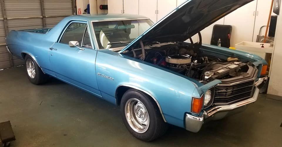 Blue classic car, hood open, in a garage.